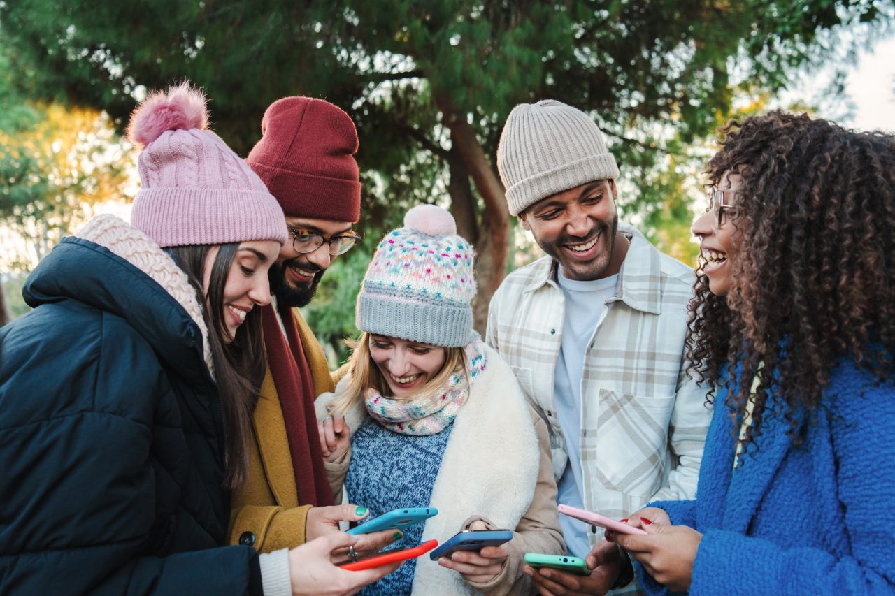group-of-multiracial-young-friends-with-coats-and-hats-smiling-and-watching-the-social-media